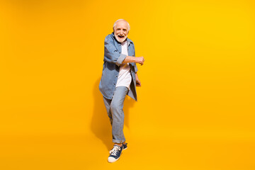 Full length body size of cool grandfather dancing feeling young in jeans jacket isolated on vivid yellow color background