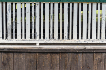 picket guide fence at the edge of a wooden deck painted in white now weathered and chipped