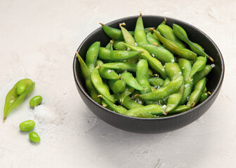 Raw edamame soya beans with salt and sauce on light gray background.
