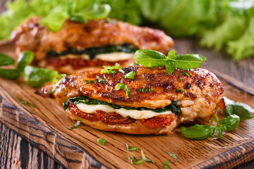 Baked chicken breast with mozzarella, sun-dried tomatoes, spinach. The meat is served on a wooden...
