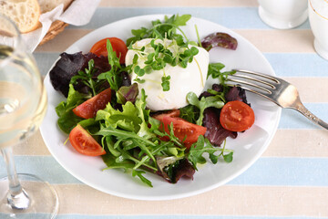 A healthy salad made from a lettuce leaves vegetables mix greens portion, arugula, tomatoes, radish sprouts and mozzarella cheese, olive oil and fresh bread, and a glass of white wine
