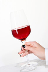 Young woman holding glass of rose wine on white background. Hand with black polish.