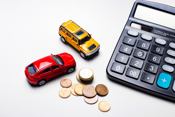 On a light gray background, red and yellow cars, a black calculator and coins. Business concept