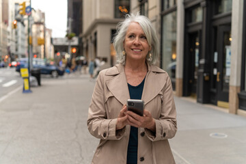 Fototapeta premium Mature caucasian woman in city walking street using cellhpone