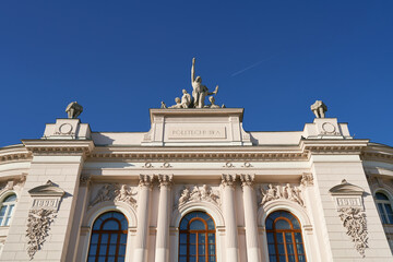 Facade top of the main building of Warsaw University of Technology on blue sky background with flying plane. Warsaw, Poland. - obrazy, fototapety, plakaty