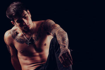 Young man with tattoos sitting with a pensive expression.