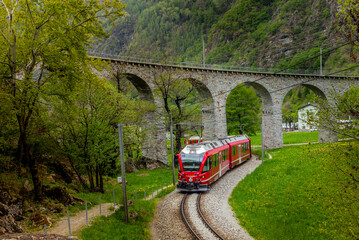 The red train on the circular viaduct bridge near Brusio on the Swiss Alps in Spring
