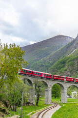 Naklejka premium The red train on the circular viaduct bridge near Brusio on the Swiss Alps in Spring