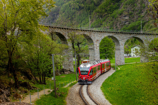 The red train on the circular viaduct bridge near Brusio on the Swiss Alps in Spring