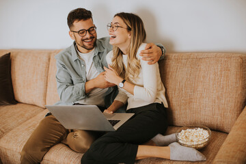 Young couple using laptop together while sitting on sofa at home