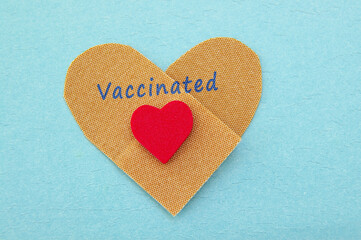 Heart shaped bandage and small red heart with Vaccinated text for COVID-19