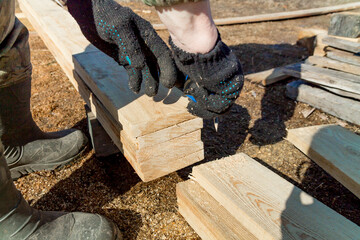 carpenter hands takes measures of wooden boards on construction site