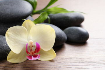 Fototapeta na wymiar Spa stones, beautiful orchid flower and bamboo sprout on wooden table, closeup. Space for text
