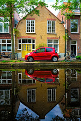 Fototapeta na wymiar Red car on canal embankment in street of Delft. Delft, Netherlands