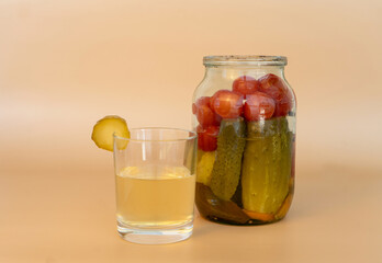 Jar with canned cucumbers and tomatoes on a beige background. A glass of brine.