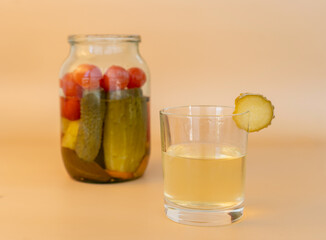 Jar with canned cucumbers and tomatoes on a beige background. A glass of brine.