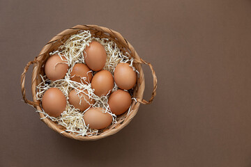 Obraz na płótnie Canvas Natural healthy nutrition and organic food concept. Raw brown chicken eggs in a basket. Top view and brown background