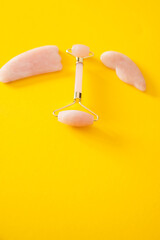 Pink Gua Sha massager roller tool and quartz stones isolated on vibrant yellow background. Facial massage kit.