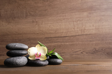 Obraz na płótnie Canvas Spa stones, beautiful orchid flower and bamboo sprout on wooden table. Space for text