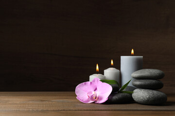 Spa stones, orchid flower, burning candles and bamboo sprout on wooden table. Space for text
