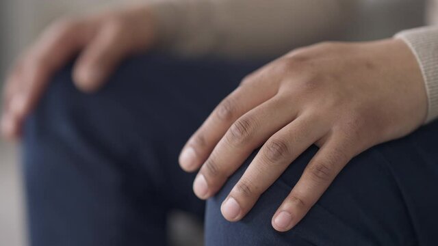 Male African American palms putting on knees in jeans. Unrecognizable young man sitting indoors waiting patiently. Close-up hands