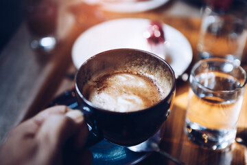 Close up of man hands enjoyed drinking and holding coffee cups over a cake cup on wooden table in the Cafe.