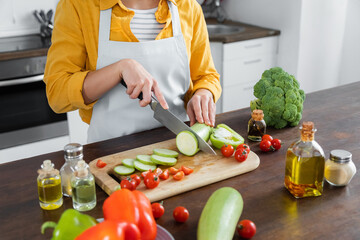 cropped view of woman in apron cutting zucchini near cherry tomatoes on chopping board