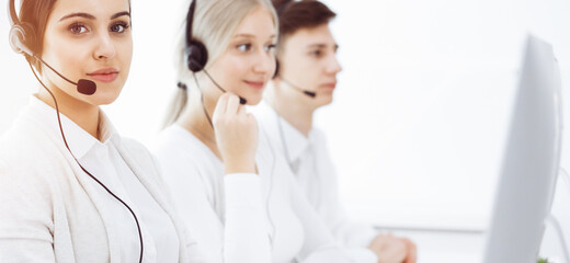 Call center in sunny office. Group of diverse operators at work. Beautiful woman in headset communicating with customers of telemarketing service