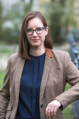 portrait of brunette woman in a suit with glasses standing outside