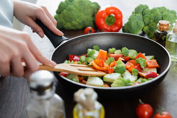 partial view of woman mixing sliced vegetables on frying pan with spatula