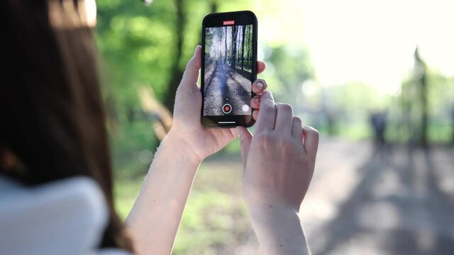 young girl in a cap shoots video on the phone in the park on a sunny spring evening slow motion
