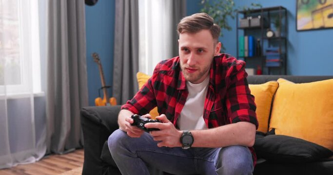 Teenager student boy playing game with joystick, enjoying sitting on sofa in living room at home, lad play the game console large tv in room.