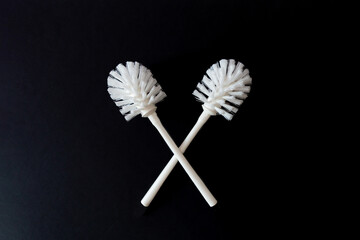 A pair of white toilet brushes on a black background. Copy space. Sanitary cleaning concept