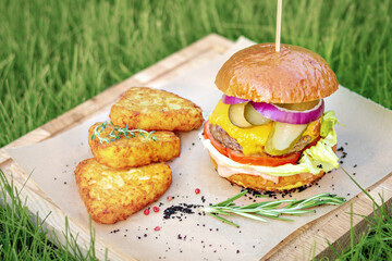 Burger with cutlet, cheese, red onion, tomato and potato nuggets. Served on a wooden board, in nature, close-up