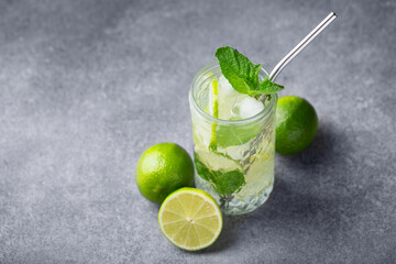 Mojito cocktail with lime and mint in a highball and a metal tube on a background of gray stone