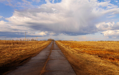 natural landscape yellow field and blue sky with clouds, concrete road through the field goes into the horizon