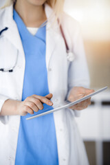 Unknown woman-doctor standing in sunny clinic and using tablet pc, close-up. Data and best service in medicine