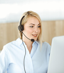 Blonde business woman sitting and communicated by headset in call center office. Concept of telesales business or home office occupation