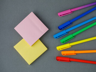 Stationary flat lay. Colored bright rainbow pens, yellow and pink square sticky paper sheets lying on grey background. Drawing education learning colors concept. Horizontal, copy space, trendy color