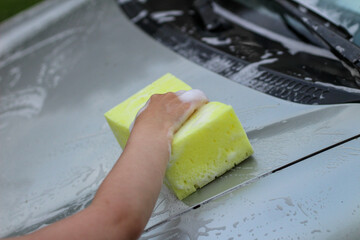 A small child's hand with a foam sponge washes the hood of the car