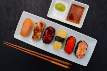 The sushi set is a famous Japanese dish, put on a ceramic plate, beautifully arranged on a black background.