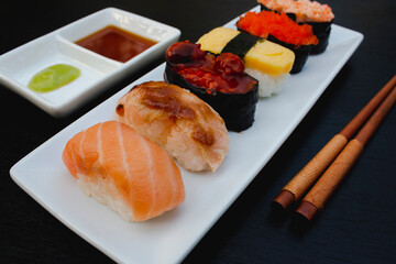 The sushi set is a famous Japanese dish, put on a ceramic plate, beautifully arranged on a black background.