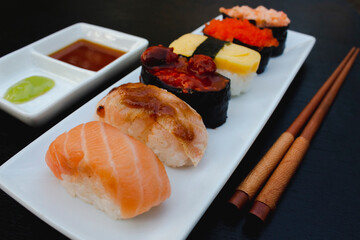 The sushi set is a famous Japanese dish, put on a ceramic plate, beautifully arranged on a black background.