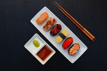 The sushi set is a famous Japanese dish, put on a ceramic plate, beautifully arranged on a black background.