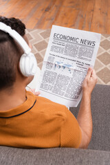 Naklejka premium overhead view of man in wireless headphones reading economic news on blurred foreground
