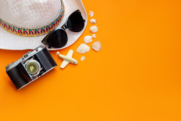 Stylish female straw white hat, black sunglasses, old vintage retro camera, toy plane and seashells isolated on a bright color orange background. Top view. Summer vacation travel concept. Copy space