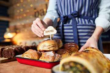 Sales Assistant In Bakery Putting Homemade Label Into Stack Of Freshly Baked Baked Cinnamon Buns