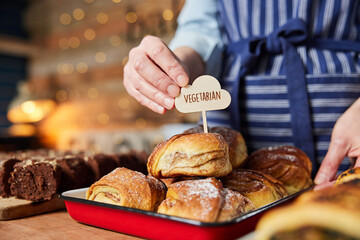 Sales Assistant In Bakery Putting Vegetarian Free Label Into Freshly Baked Baked Cinnamon Bun