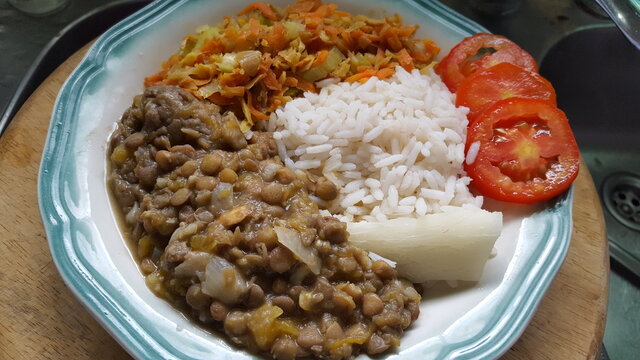 A plate of Trinidad and Tobago's traditional dish of lentil peas/beans, rice cabbage, carrot, and salted fish,  cassava, and sliced tomato. 
