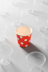 Eco friendly red paper cup surrounded by plastic cups on a gray table. Plastic-free concept, biodegradable tableware, recyclable.